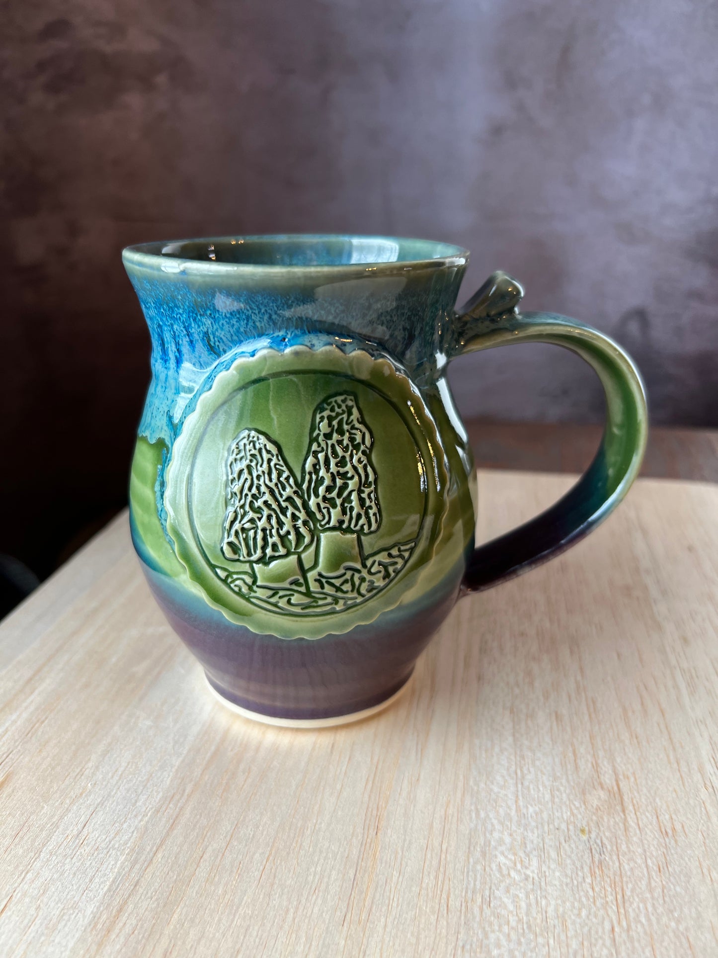 Left-handed ceramic mug in purple, green and blue with a medallion depicting 2 Morel mushrooms