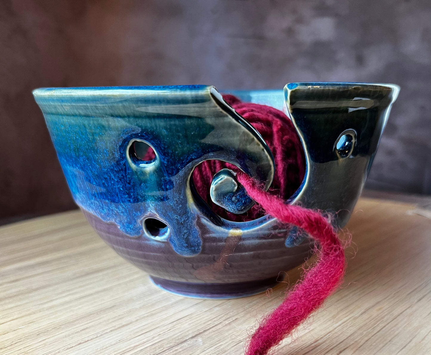 A handmade ceramic yarn bowl with a spiral design, in blue and green colors, with a red yarn bowl in the foreground.