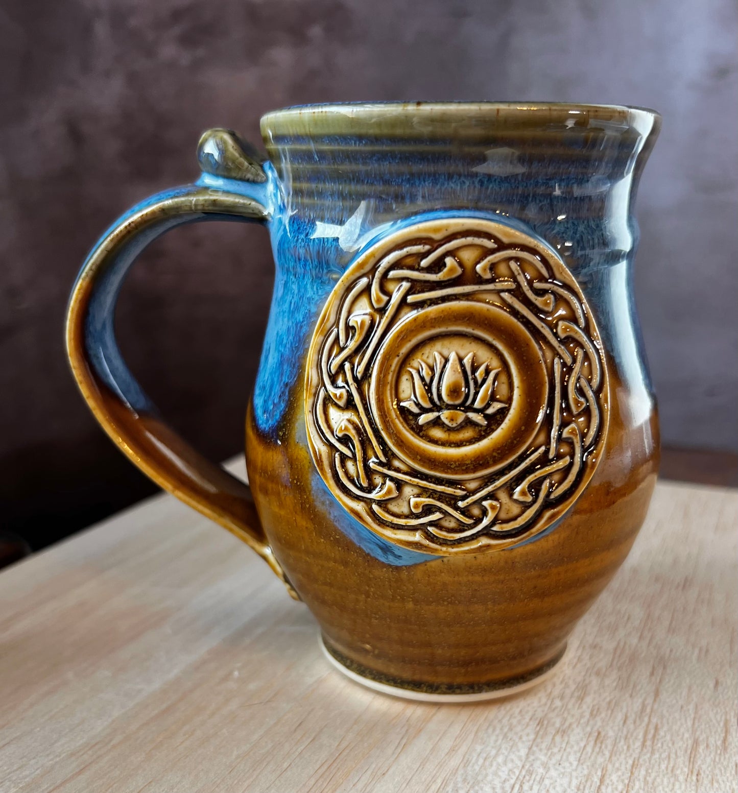 Ceramic mug with Celtic knots and a lotus flower in the center. Blue and brown glazed, hand thrown pottery.