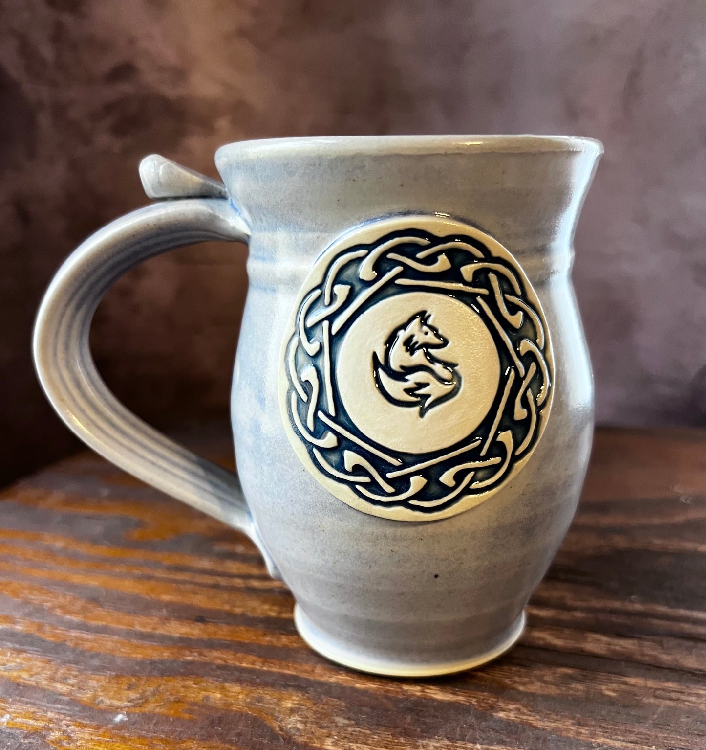 Hand thrown ceramic mug with a celtic knot circle containing a fox in the center.