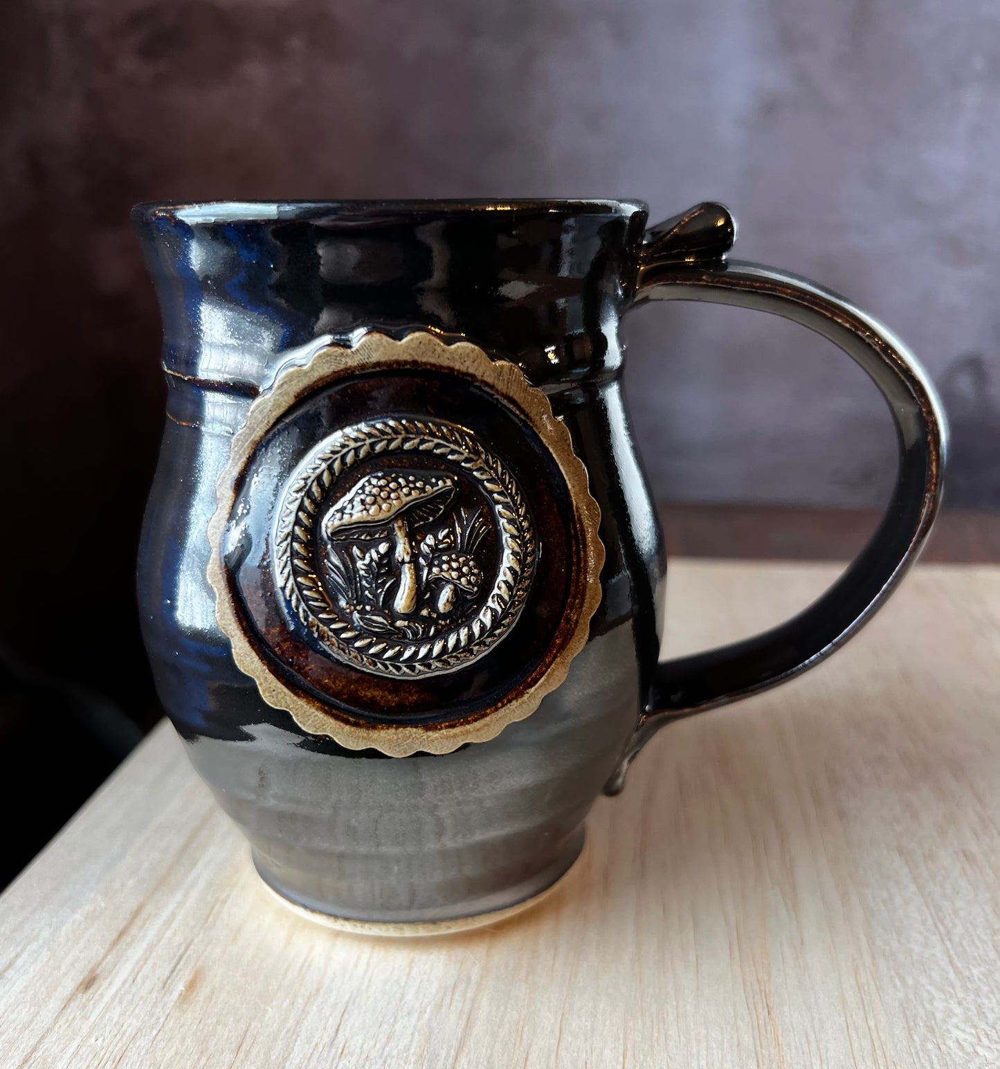 Left handed Black glazed mug with Amanita mushrooms in a medallion.