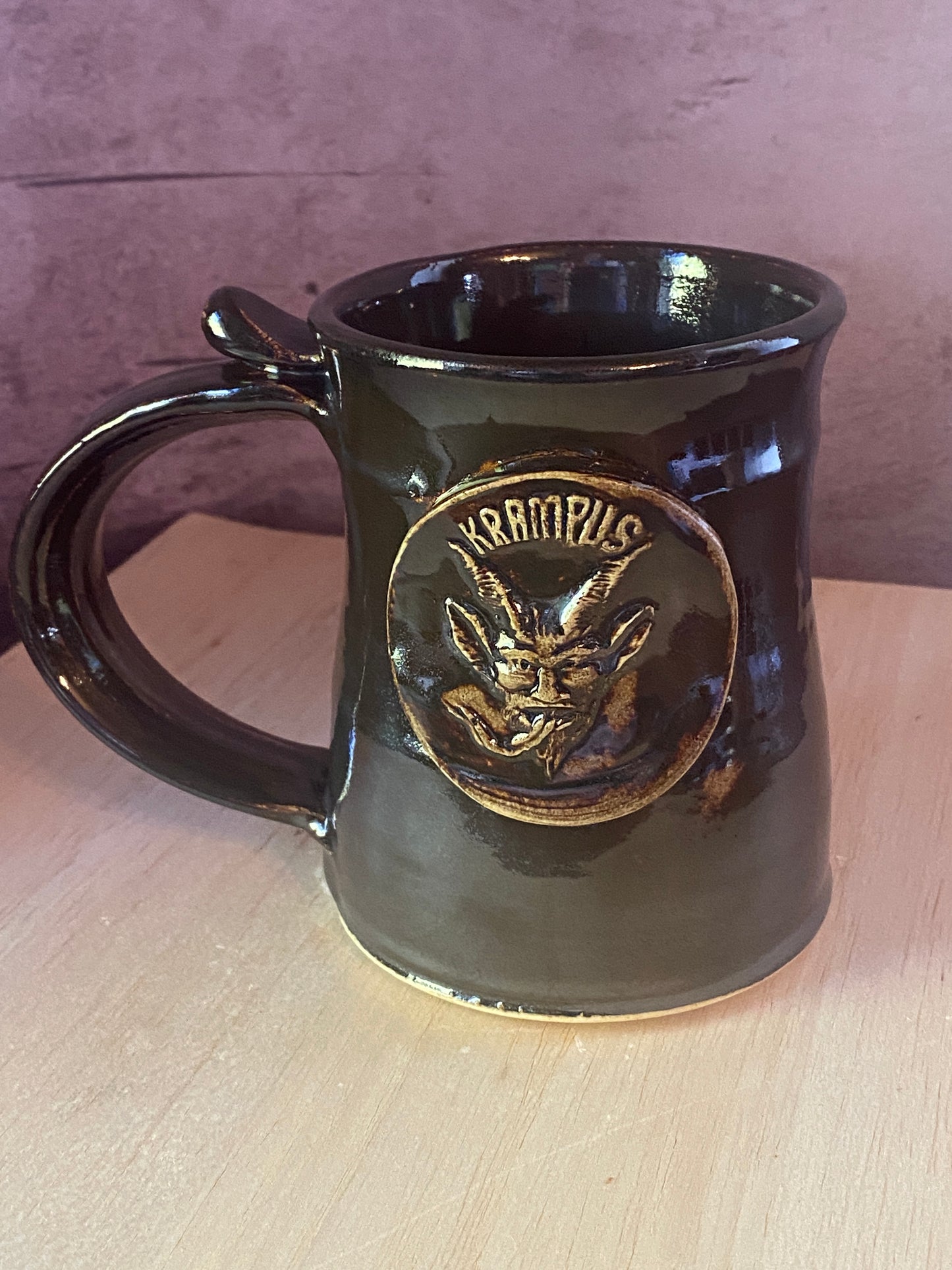 Black mug with gold emblem featuring a Krampus face medallion.