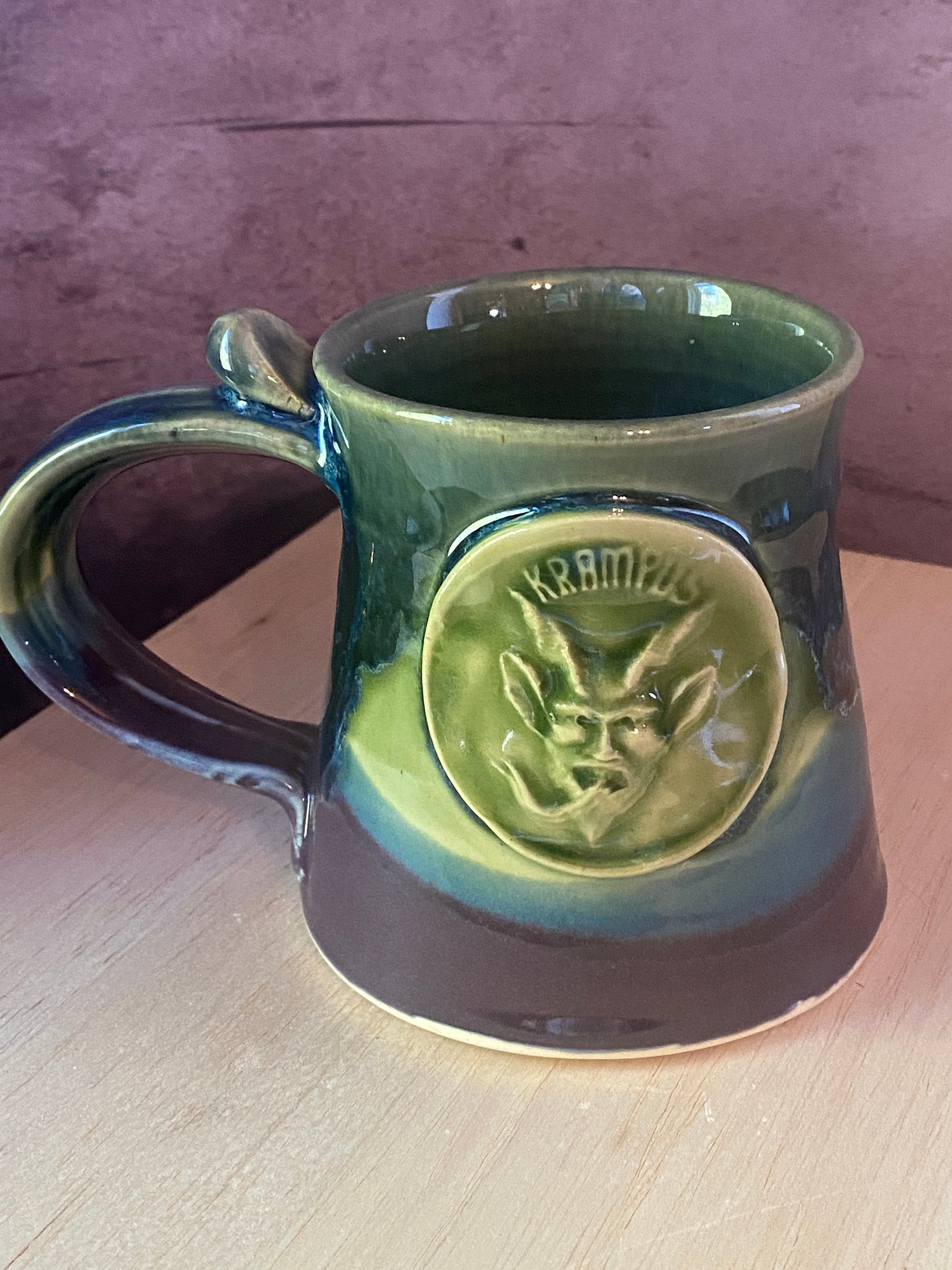 Small pottery mug with Krampus face medallion in blue green and purple glazes