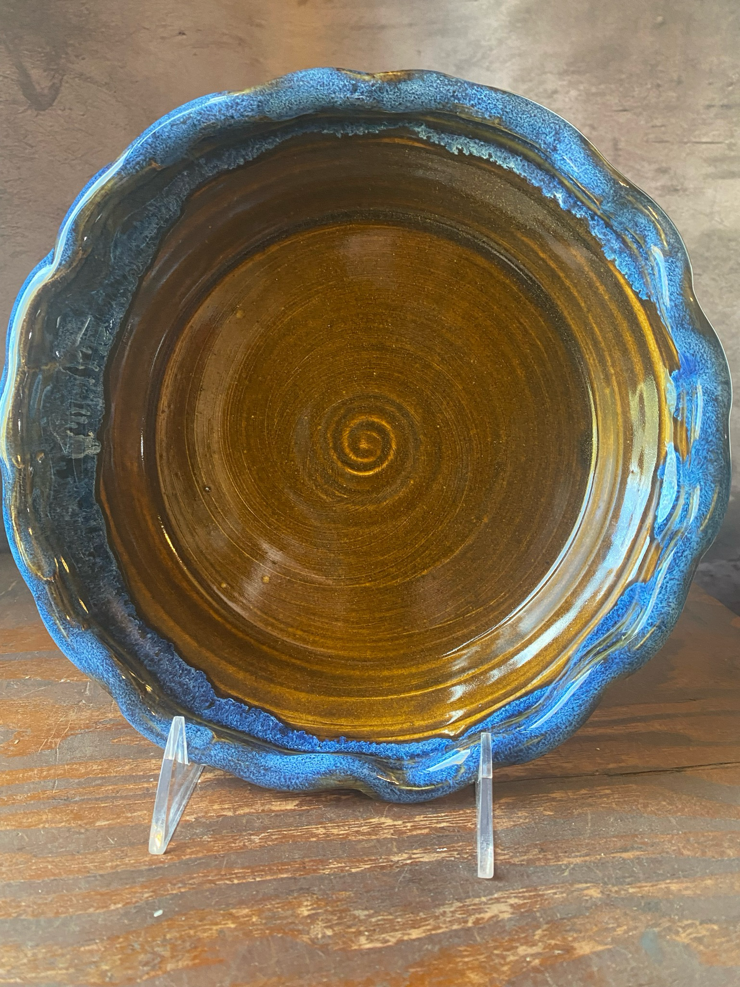 A handmade stoneware pie baker with a blue rim and a ruffled edge and brown glazed center. 