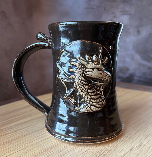 A black ceramic tankard with a sculptural dragon design on the side