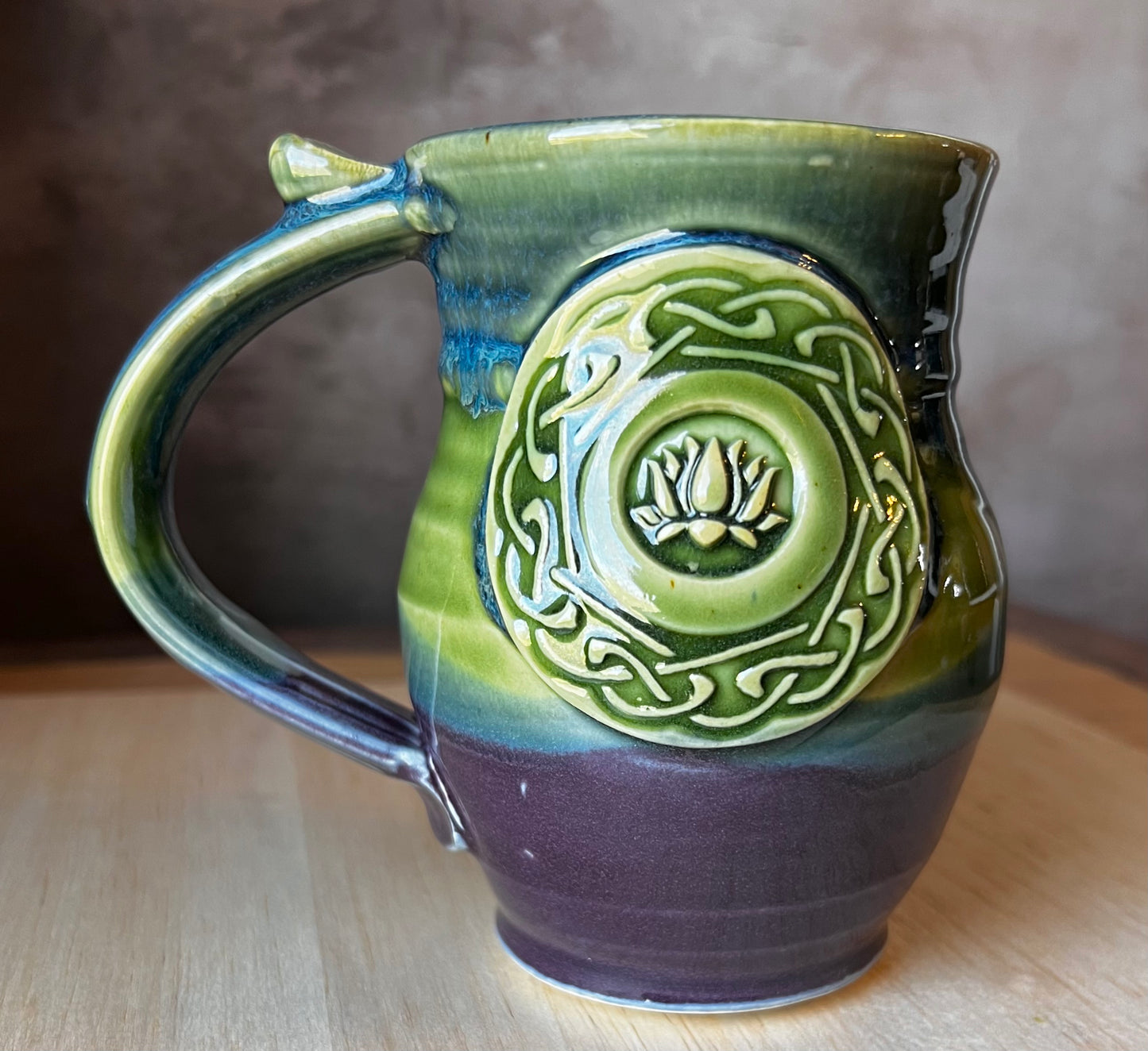 A handcrafted ceramic mug with a lotus medallion and Celtic knotwork in black, gold, and green colors. Perfect for after yoga tea relaxaion.