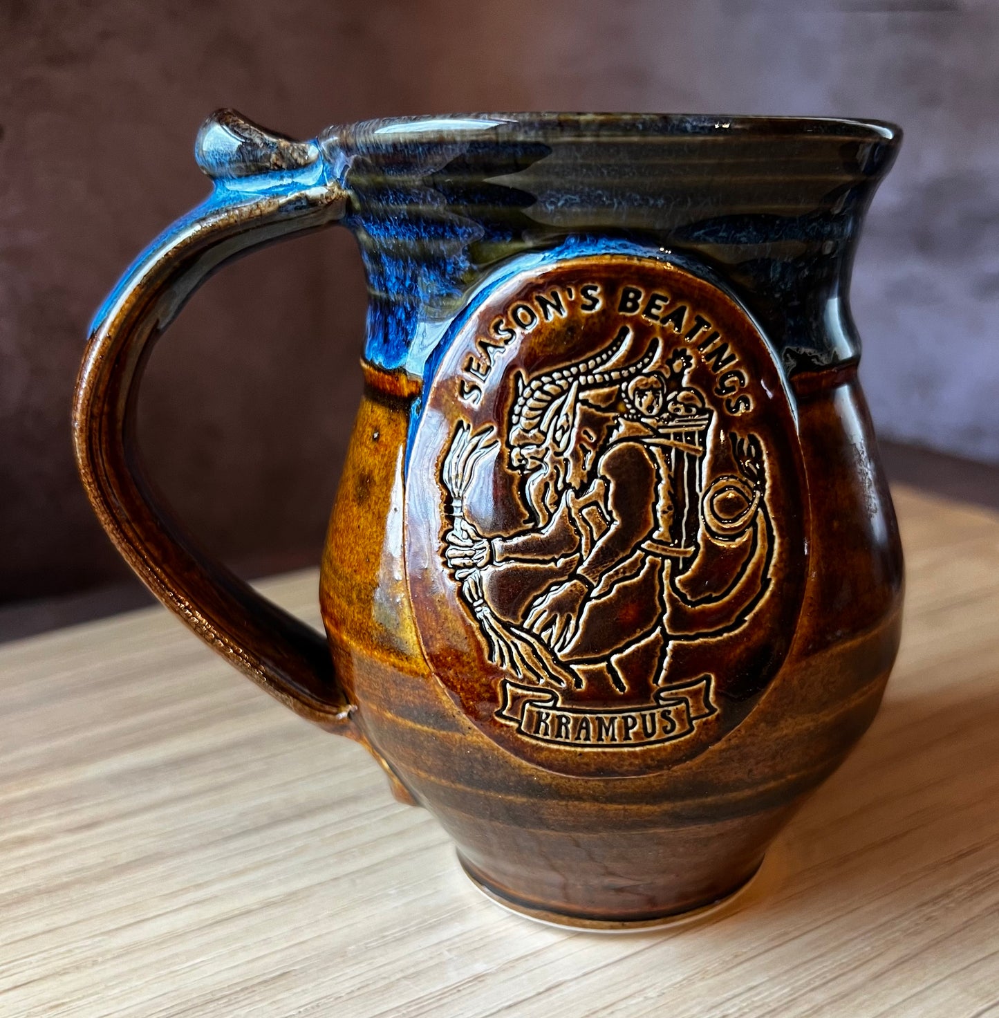 Alternative to Christmas ceramic mug with Krampus that says Seasons Beatings. The hand thrown pottery is glazed in blues and browns.