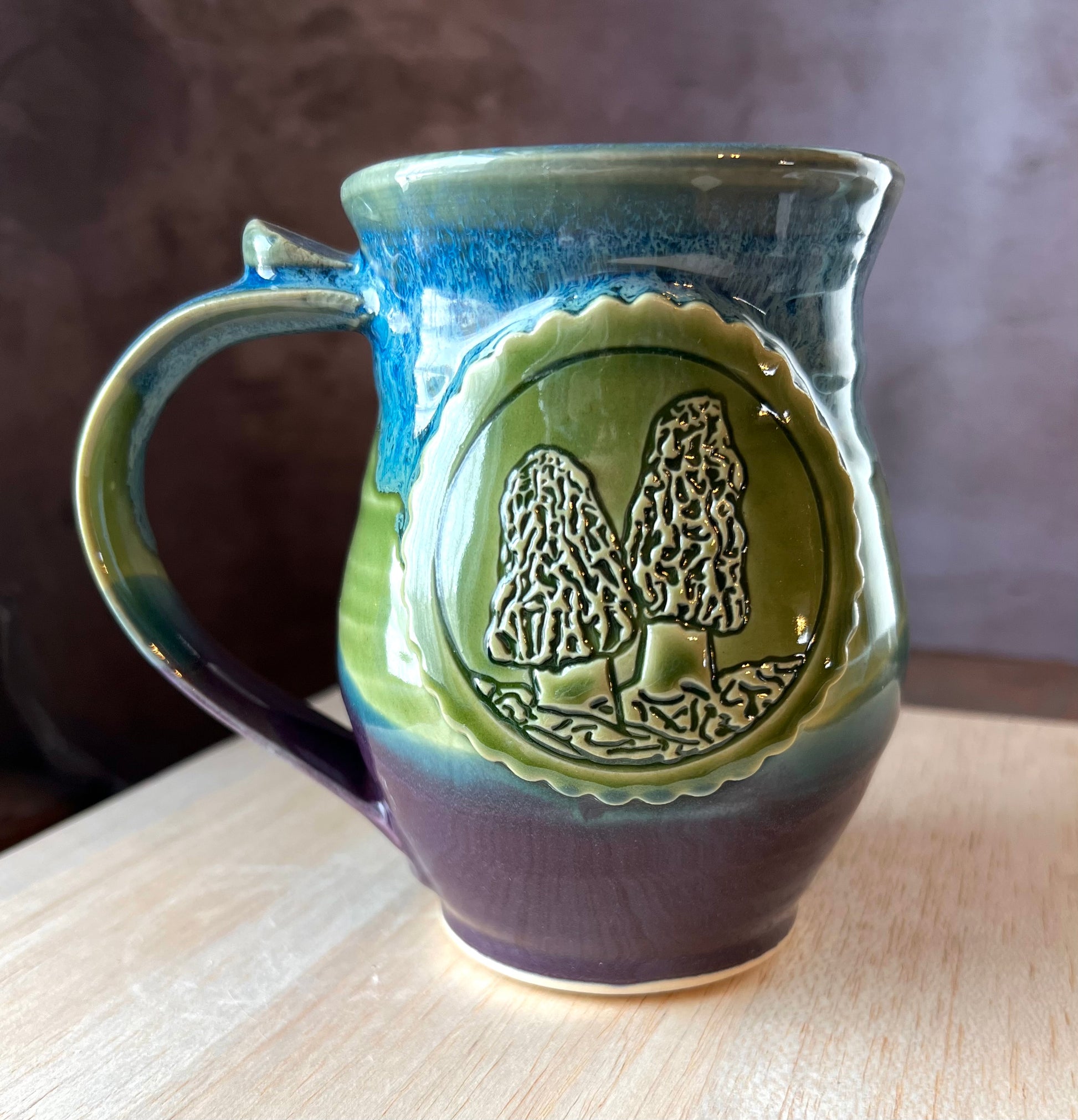 Ceramic mug with green and blue glaze and morel mushroom medallion.