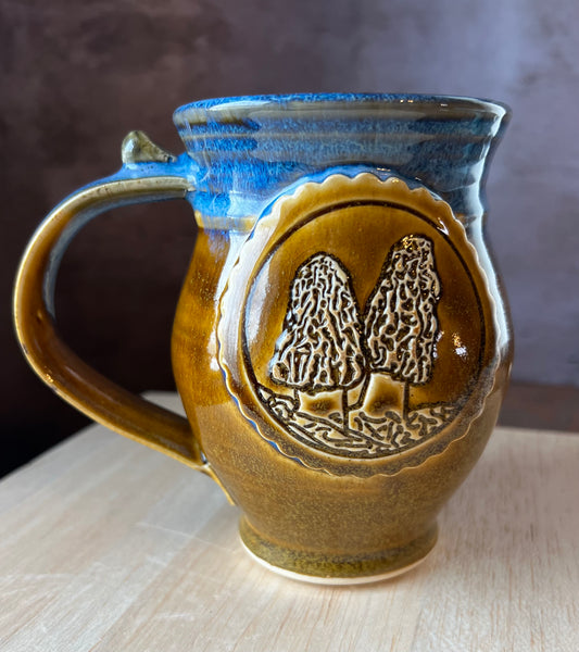 Ceramic mug with blue rim and brown body featuring a Morel mushroom medallion.