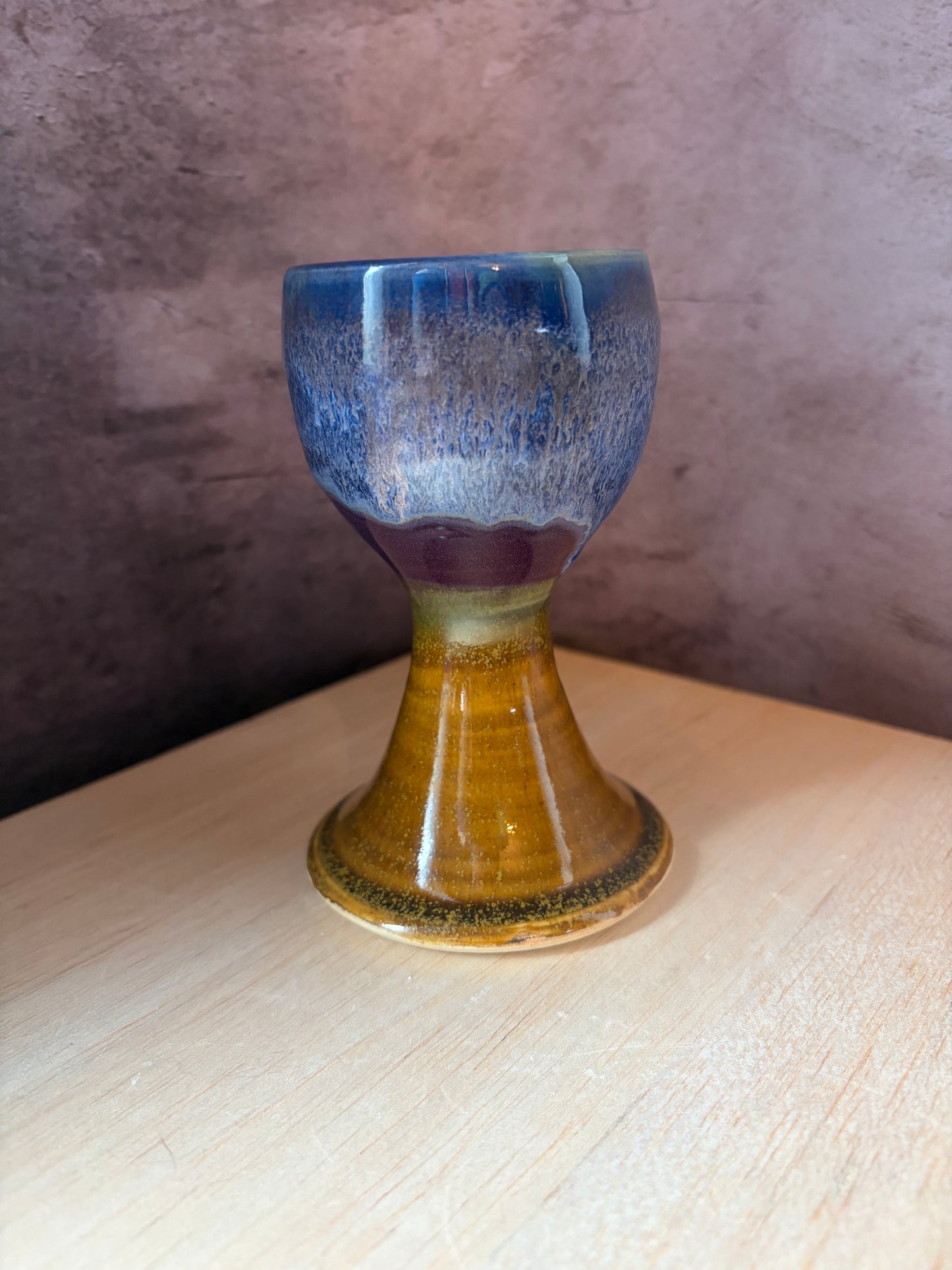 Shades of purple and blue glaze on the top of a stoneware goblet with a brown base.